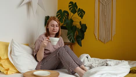 woman stretching on bed and drinking beverage