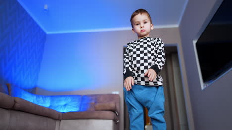 beautiful dark-haired toddler boy in checkered shirt lies on the floor. kid stands up and runs out of the room. low angle view.