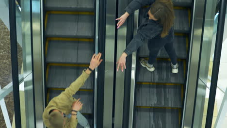 Working escalator in the mall with stairs going up and down. Girlfriend meeting her boyfriend when moving on the opposite stairs. View from top.