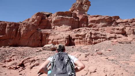 aventurero con mochila caminando por el desierto árido, valle del arroyo, montañas al fondo, cielo azul, tiro de gran angular, viaje