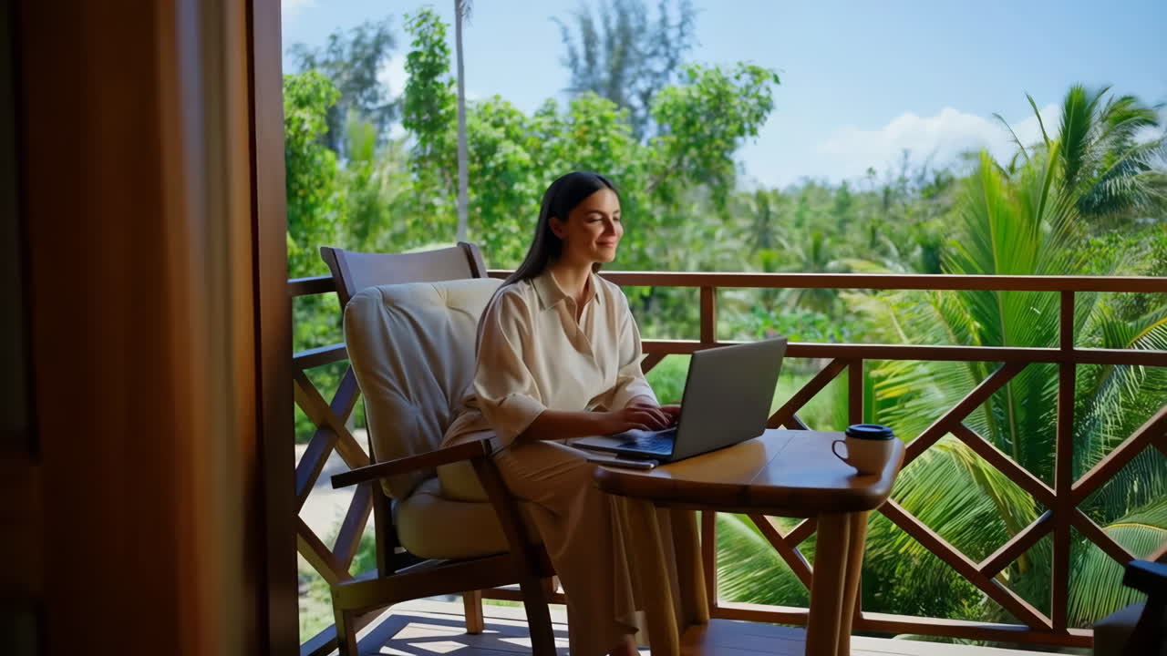 Woman working on a laptop on a tropical resort balcony