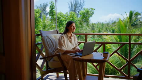 woman working on a laptop on a tropical resort balcony