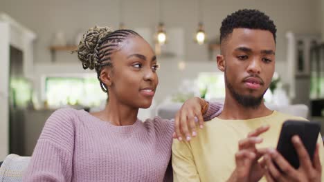 happy african american couple sitting on sofa and relaxing with tablet