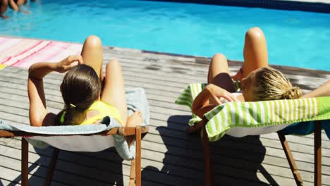 dos mujeres interactuando entre sí mientras toman el sol cerca de la piscina