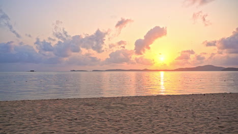 view from a deserted beach, a colorful setting sun peaks through the clouds as it slips toward the ocean horizon