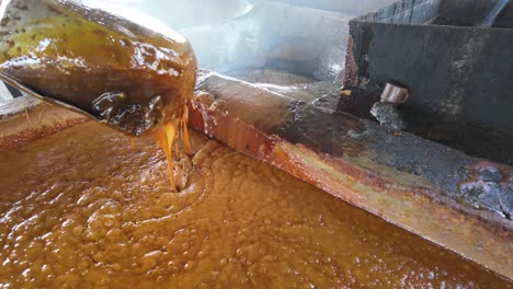 man extracting juice from boiling sugarcane for crystallized brown sugar