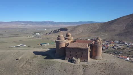 drone shot over the castle of la calahorra on top of a hill with farmlands behind