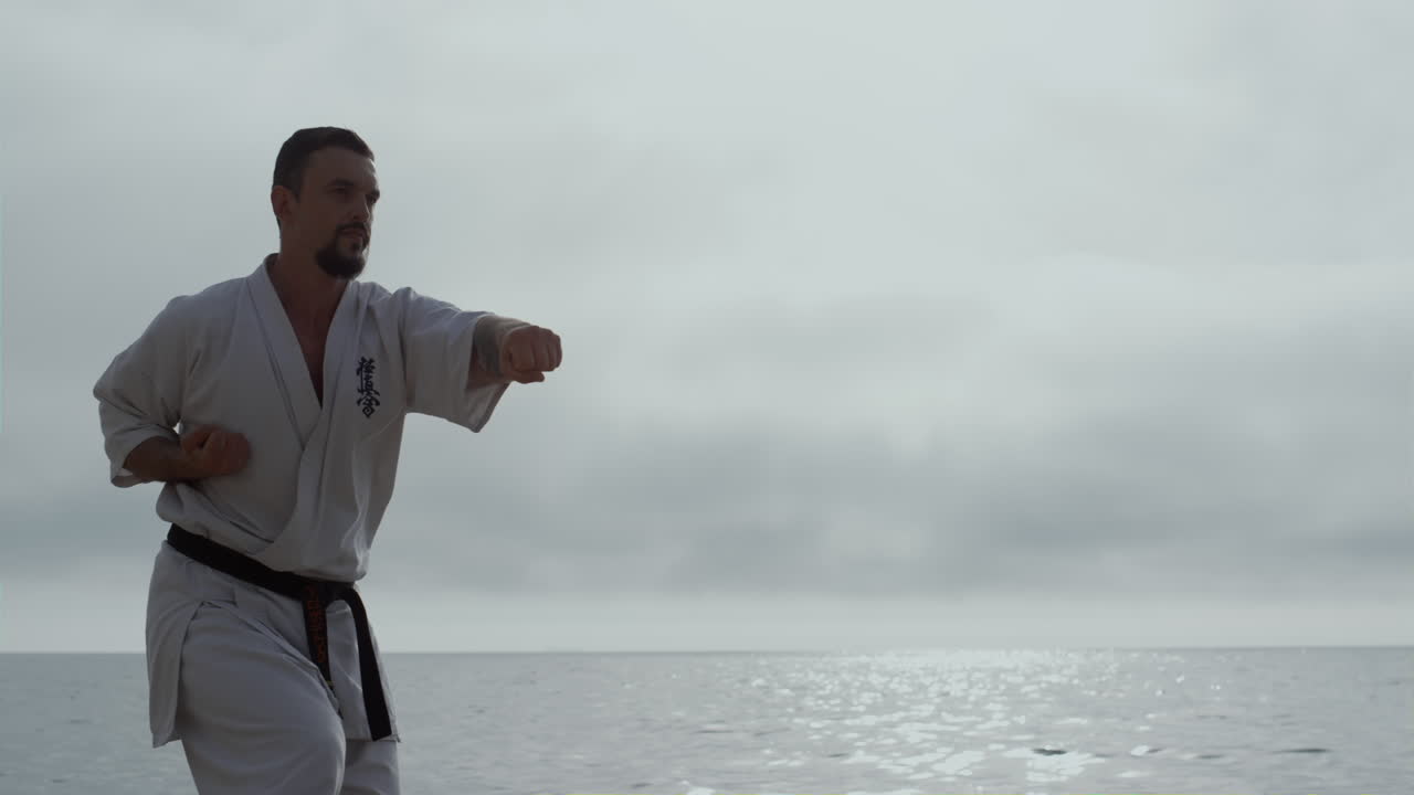deportista aprendiendo artes marciales en la orilla del mar. hombre barbudo practicando habilidades de lucha