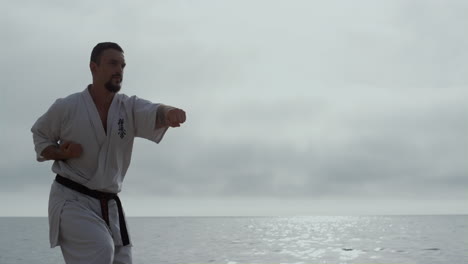 sportsman learning martial arts on seashore. bearded man practicing fight skills