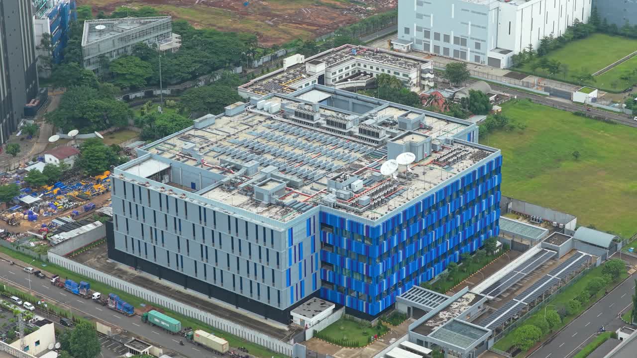 High angle view of a large, modern data center building with a distinctive blue and gray facade, showing servers and cooling systems on the roof