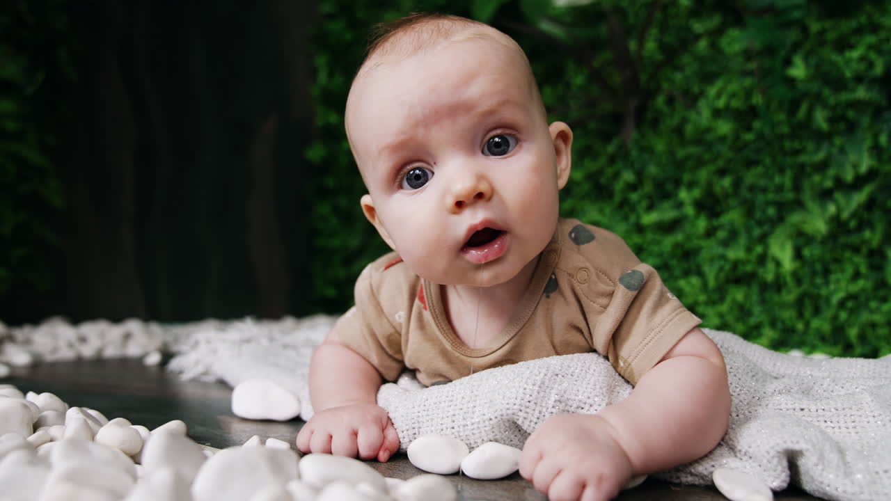 Adorable baby lies on the belly holding head up. Saliva flows from infant's mouth. Surprised child looks at camera. Close up.