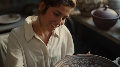 excited lady using potters wheel in pottery. woman enjoying plate with ornament