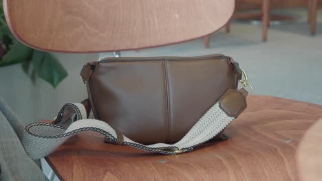 woman putting on a brown leather shoulder bag in a cafe