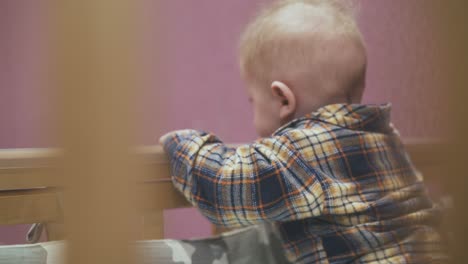 little child with blond hair crawls playing in cot in room