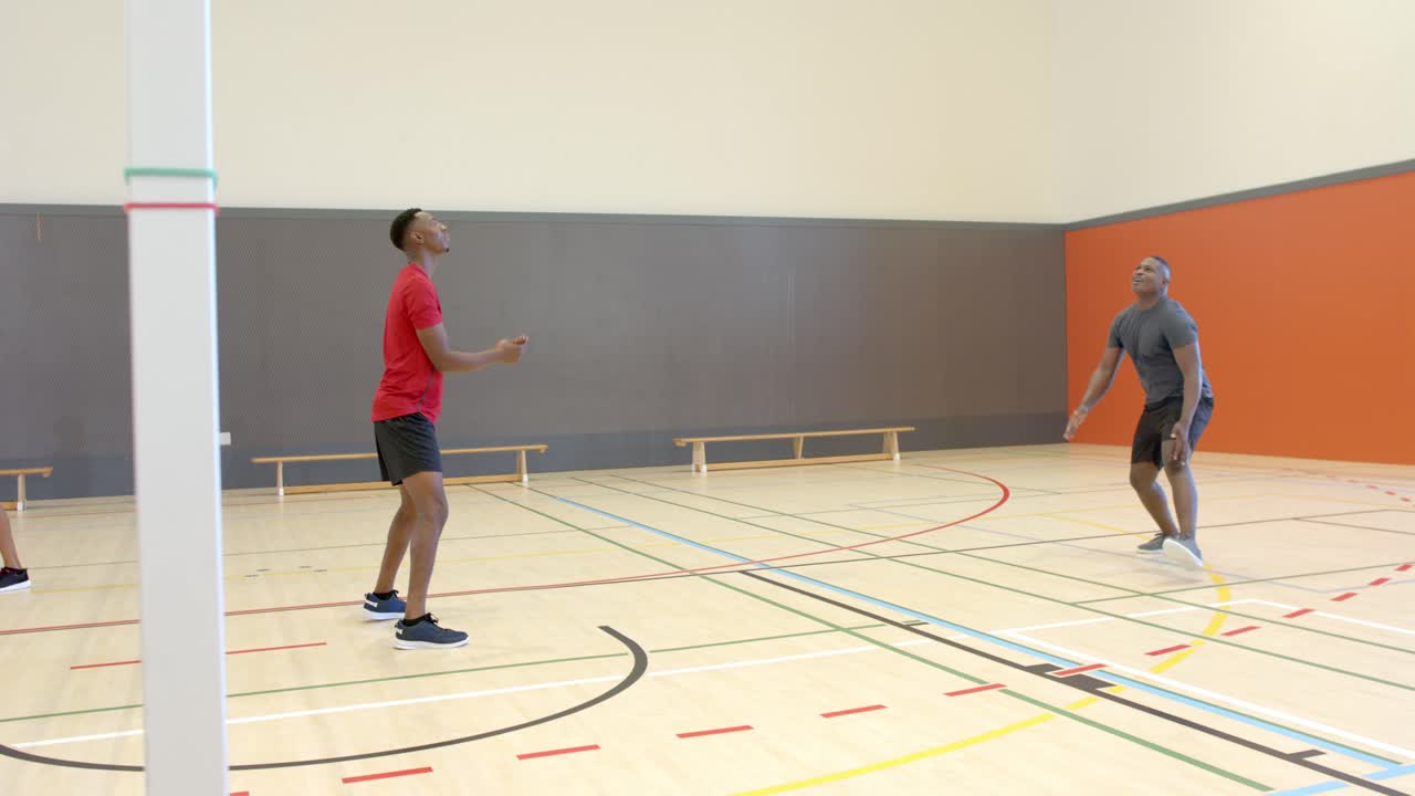 African American men tossing ball over net, passing overhead, bumping, drilling at gym