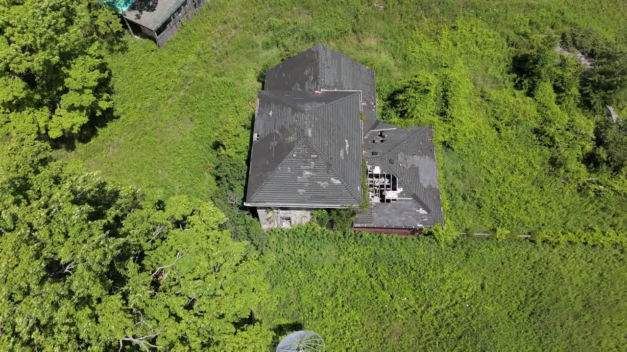 Aerial view of abandoned rural house surrounded by overgrown grass and dense green trees