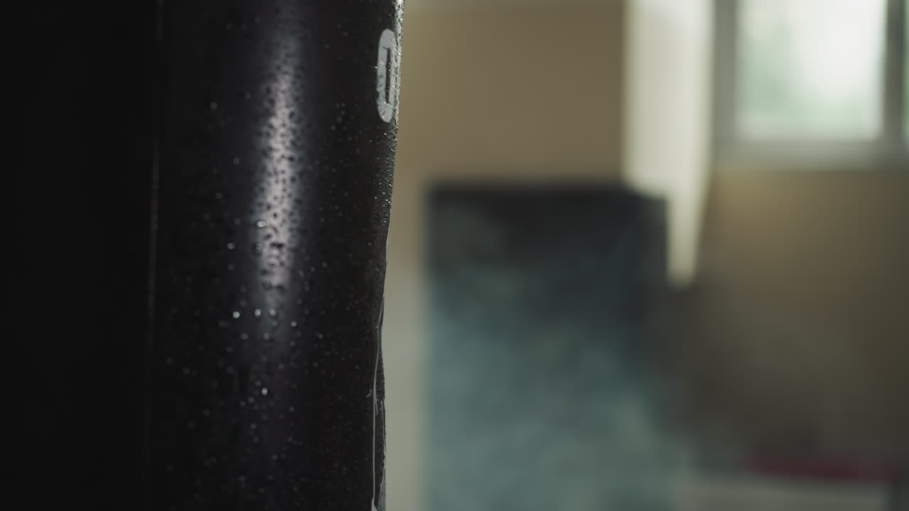 Man boxing expert using hand in glove strikes punching bag with droplets of water. Engaging in combat sports and enhancing strength in dark gym