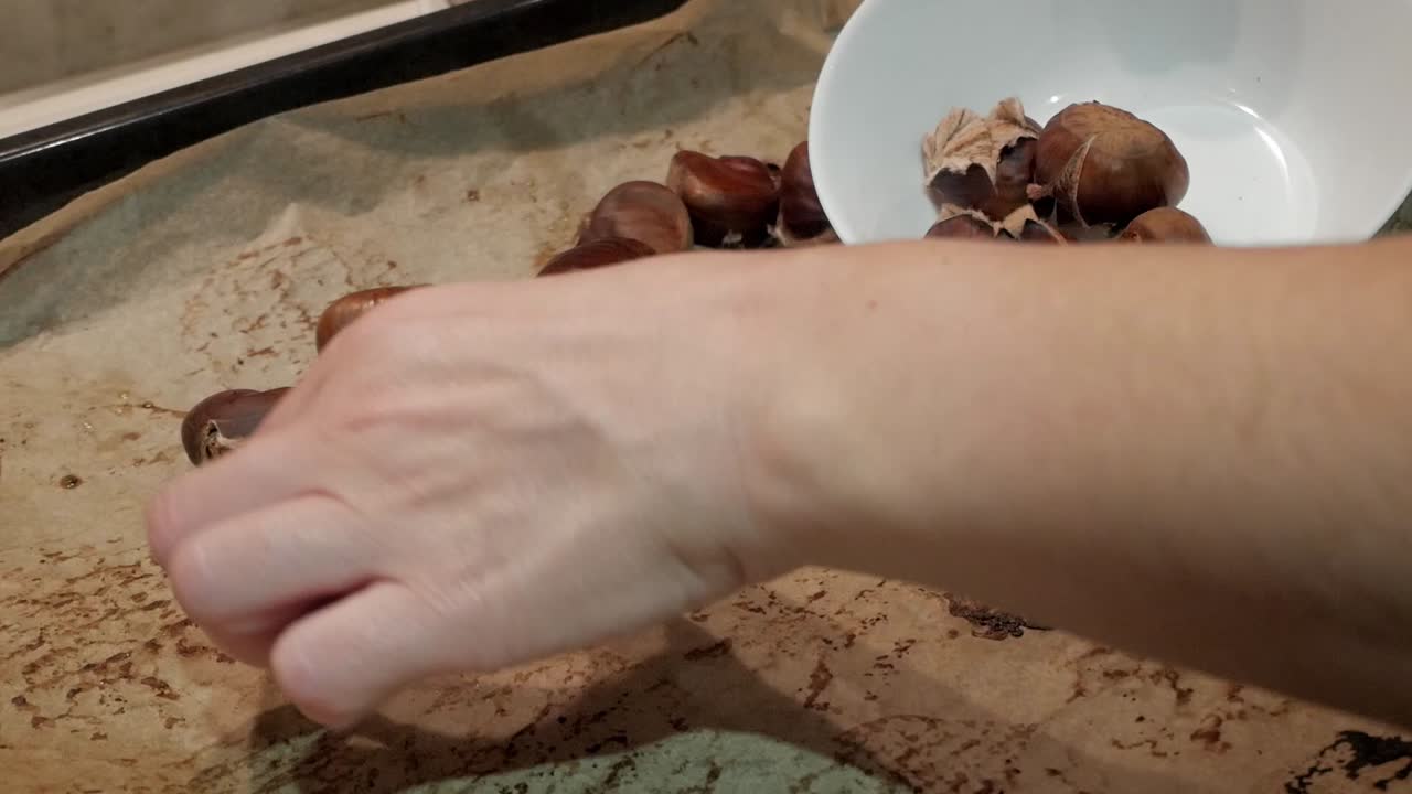 Roasted chestnuts on oven tray being picked by female hands. Christmas popular snack.