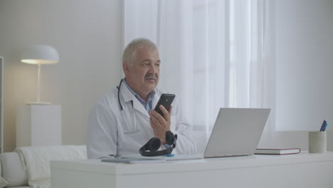 terapeuta experiente está consultando o paciente ou conversando com um colega por telefone celular sentado no escritório da clínica usando alto-falante