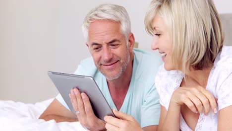 Happy-couple-lying-on-bed-using-tablet-together