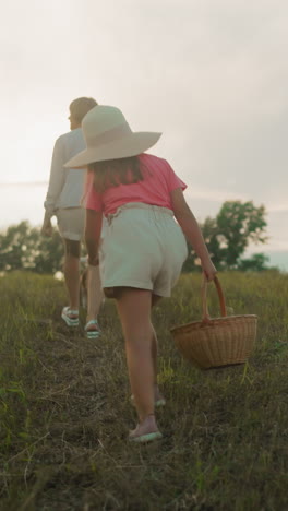 familia caminando por la colina cubierta de hierba con el perro en la cálida luz del atardecer, capturando el movimiento y la alegría, joven con sombrero conduce con la canasta, otros siguen, creando una escena al aire libre pacífica