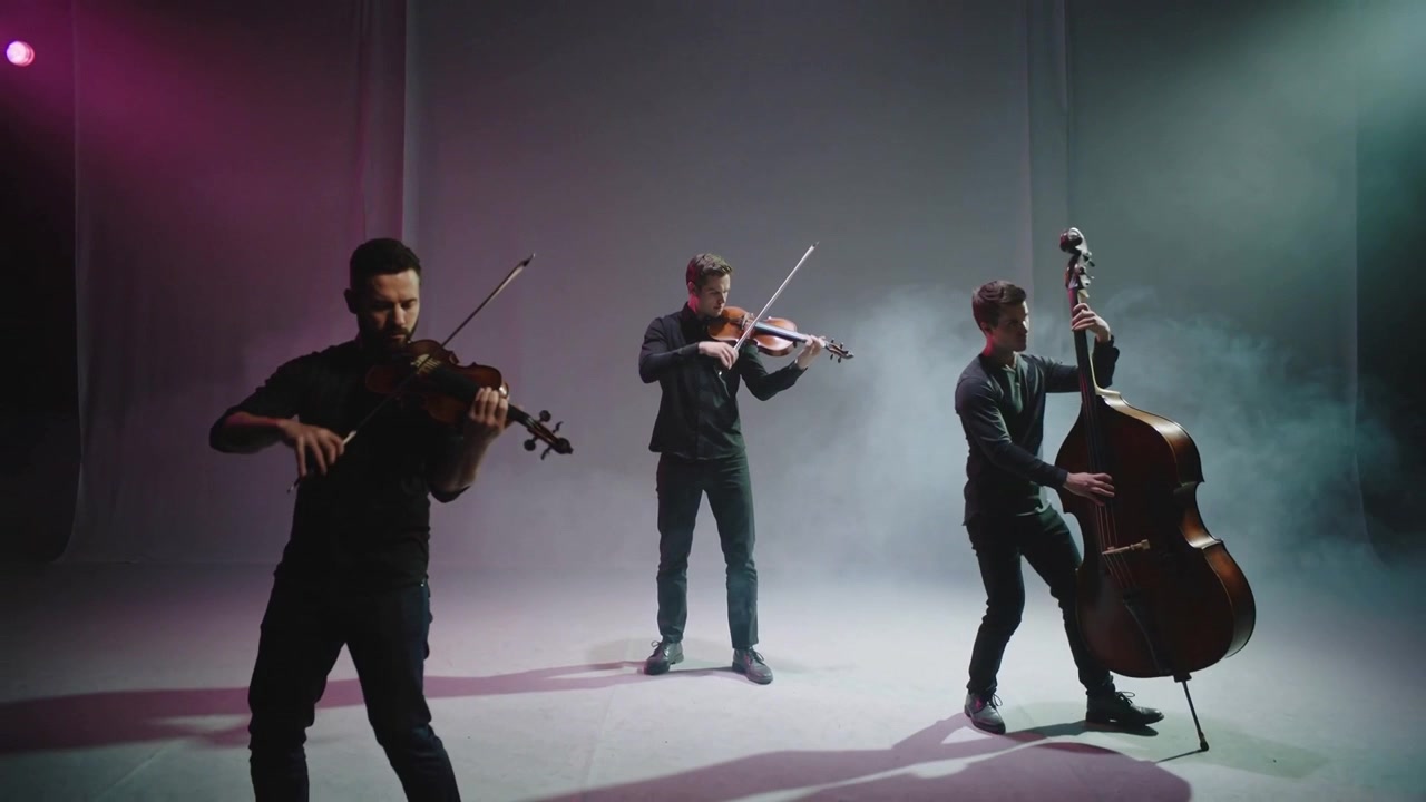 Violinista mancino che inizia a suonare con l'archetto, dando il via a un trio che suona violini e basso in studio, indossando abiti scuri.