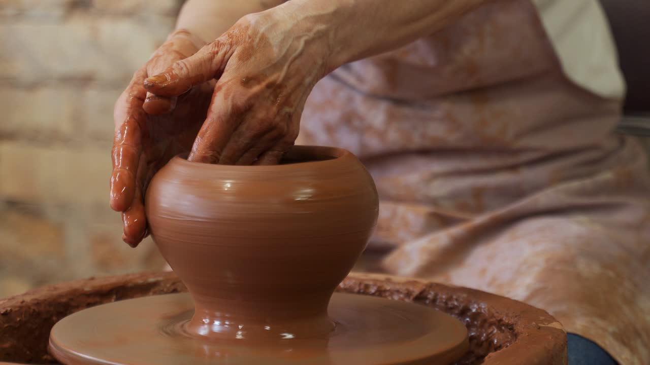 el escultor en el estudio hace un primer plano de una olla de arcilla. una mujer mayor está esculpiendo un cuenco detrás de una rueda de alfarero giratoria