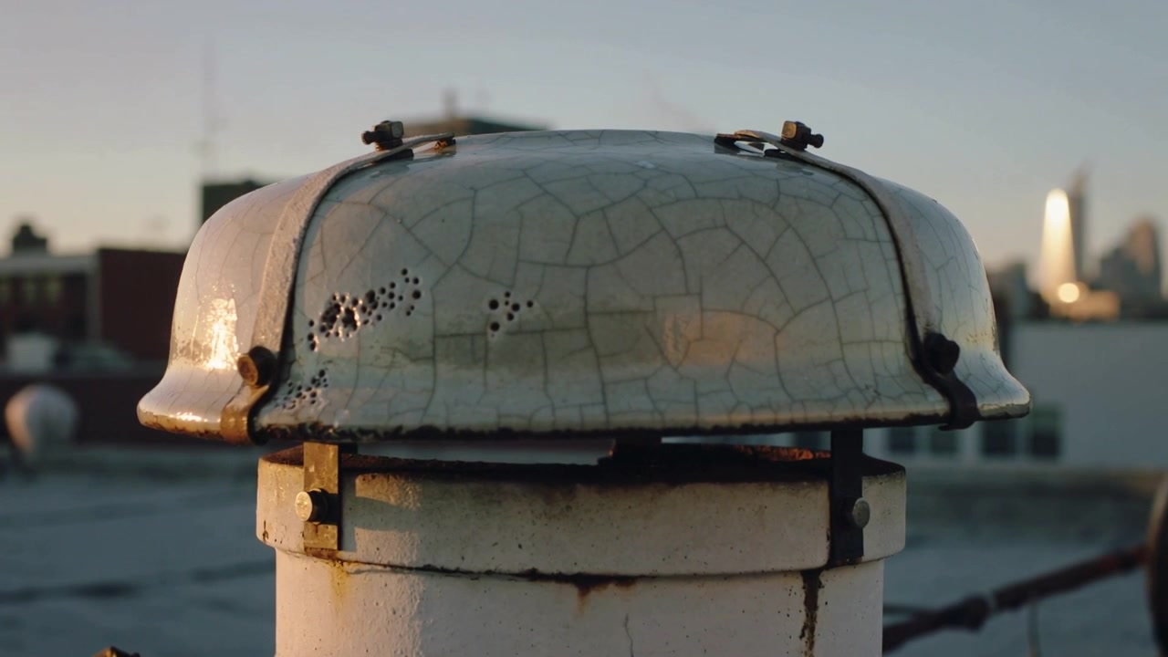 Zooming camera focusing on worn domed rooftop vent cap at rooftop, showing cracked paint and clamps