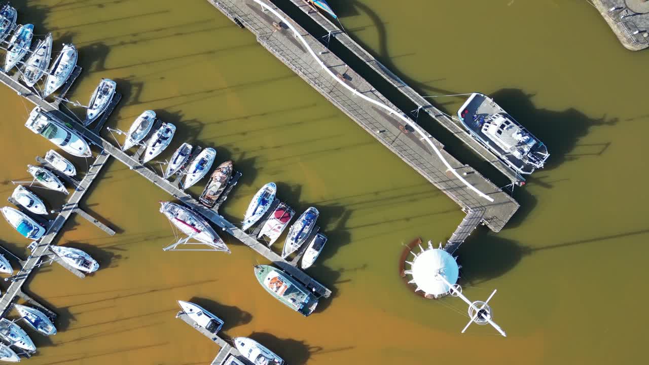 Overhead drone footage captures an array of sailboats and yachts moored at harbor at England, UK, the organized marina contrasts with serene sea during daytime