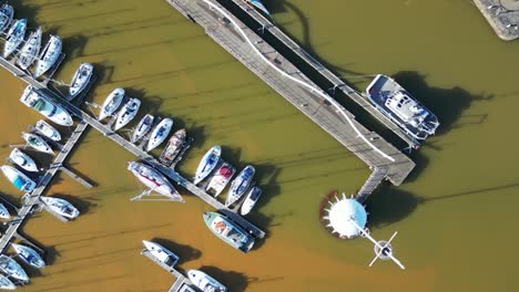 overhead drone footage captures an array of sailboats and yachts moored at harbor at england, uk, the organized marina contrasts with serene sea during daytime