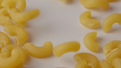 close-up of dry macaroni pieces tumbling down onto a white surface in soft light