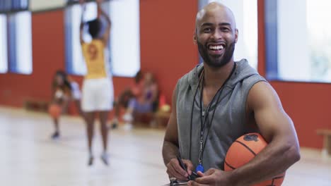 portrait of african american male basketball coach holding ball in indoor court, in slow motion