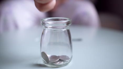 hand is putting a coin into glass jar on a blue background