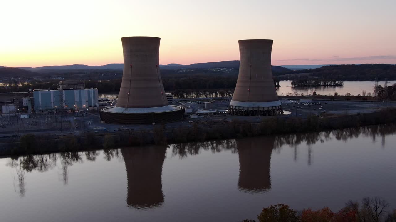 escena industrial aérea, torres de enfriamiento de la planta nuclear con frente al río al atardecer, generación de energía atómica, energía nuclear peligrosa, riesgo ambiental y concepto de contaminación