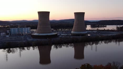 aerial industrial scene, cooling towers of nucler plant with riverfront in sunset, atomic power generation, dangerous nuclear energy, environmental risk and pollution concept