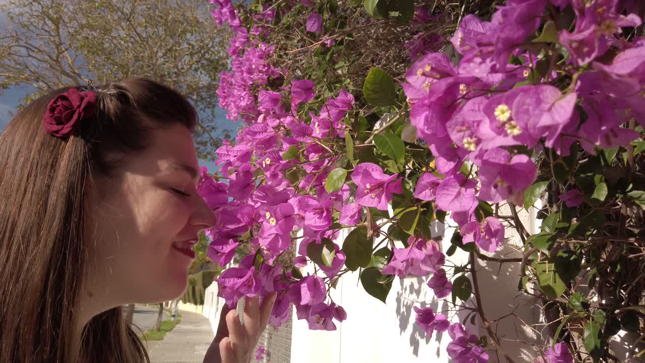 una joven sonriente huele a flores de buganvillas moradas, un primer plano lento