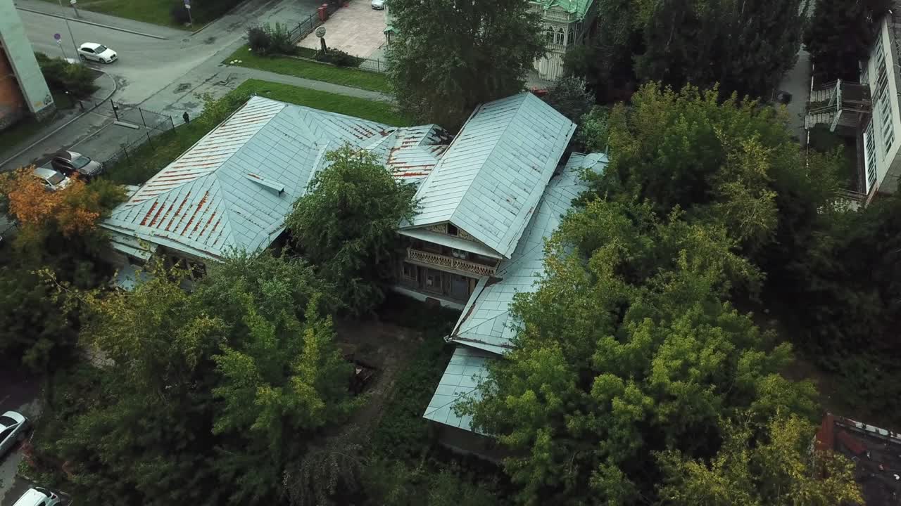 Aerial drone view of old wooden house among green trees in a summertime in a countryside area. Stock footage. Picturesque nature in the village and old ugly house