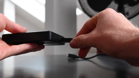 an electronice device user plugs a black cable into an external hardrive to use the storage