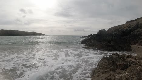 Slow-motion-foaming-ocean-tide-crashing-against-rugged-Welsh-waterfront-at-sunrise