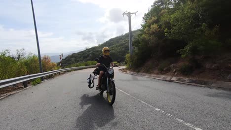 motorcycle rider with helmet transporting black kiteboard on asphalt road in vietnam at summer