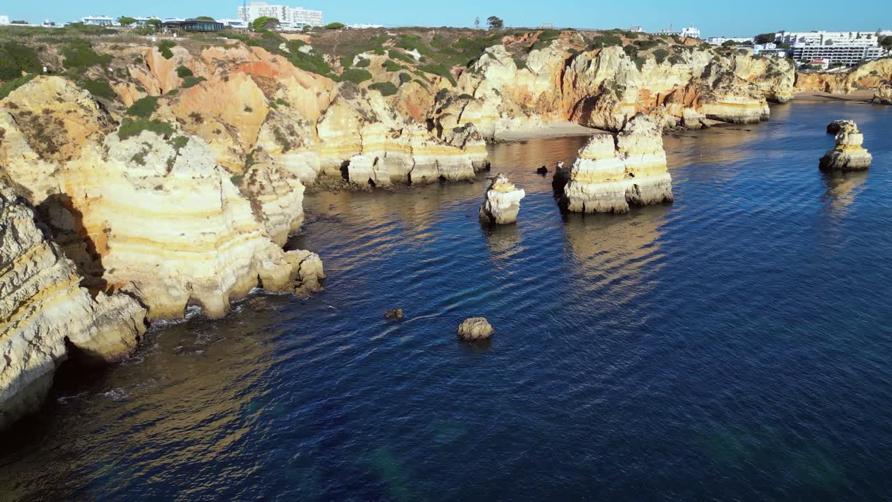 Low coastal aerial: Steep golden ocean cliffs show shoreline erosion