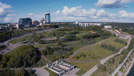 aerial flyover the dark blue north saskatchewan river, flyby the louise mckinney public lush park chinese garden pavilion and oval track birds eye view on a hot summer day with cumulus cloud coverage