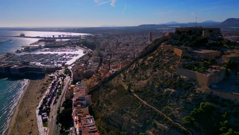 Toma-Aérea-De-Drones-De-Playa-Del-Postiguet-Y-Castillo-De-Santa-Barbara-En-Alicante-España-Con-El-Puerto-Deportivo-Y-Pequeños-Veleros-En-El-Fondo