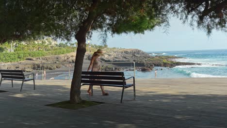 joven mujer atractiva camina y se sienta bajo el árbol cerca del océano atlántico