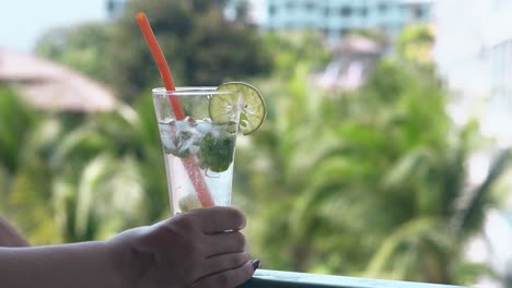 woman relaxes on hotel balcony with frozen mojito in hand