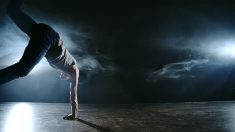 male dancer performs a stunt jump with a rotation back and a revolution in the scene in the smoke in the spotlight. modern ballet