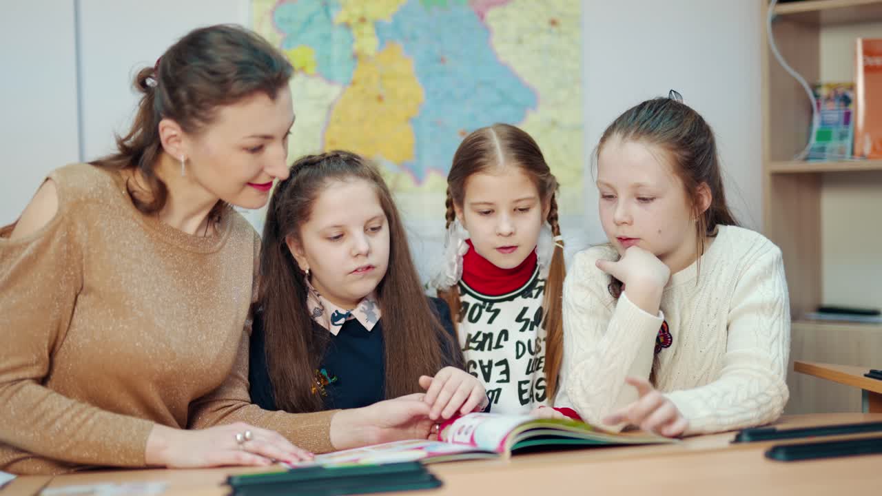 Learning process at primary school. Young female teacher sitting together with little schoolgirls and studying at school. Education concept.