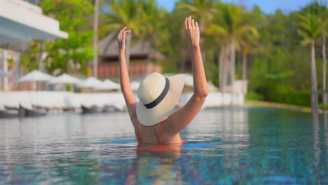 Una-Mujer-De-Espaldas-A-La-Cámara-Se-Aferra-A-Los-Bordes-De-Su-Sombrero-Para-El-Sol-Mientras-Reacciona-A-La-Alegría-De-Estar-De-Vacaciones