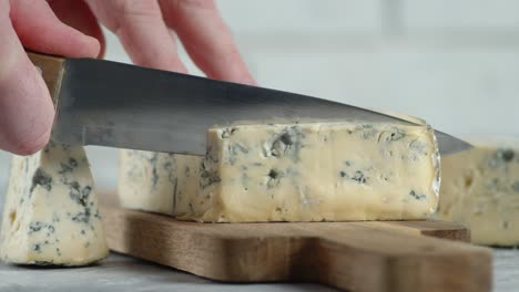 mano masculina con un cuchillo cortó un pedazo de queso brie.