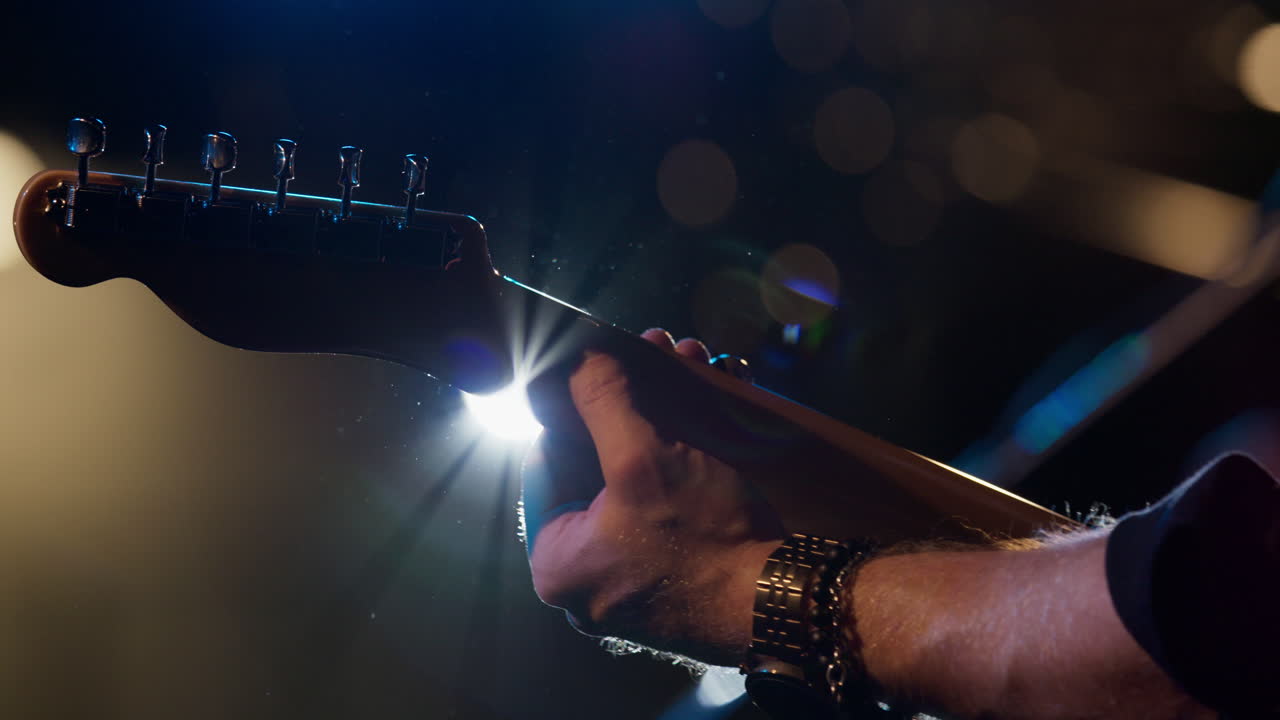 Musician plays electric guitar with bright lights and lens flare. Slow motion shot close up.